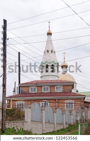 Split-level wooden house and church of the Falling Asleep of the Mother of God icon against cloudy sky background with numerous wires of power line in foreground. Gorodets,  Russia.
