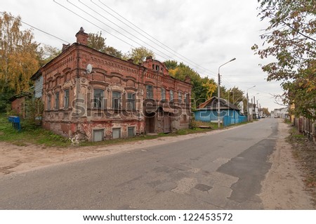 Old two-storeyed brick mansion and other buildings on street with road before against cloudy sky background. Gorodets, Nizhegorodsky region, Russia.