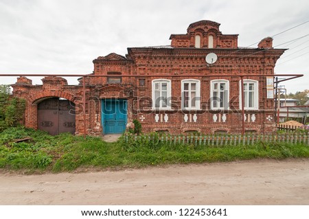 Old brick mansion with metal gate, palisade and road before against cloudy sky background. Gorodets, Nizhegorodsky region, Russia.