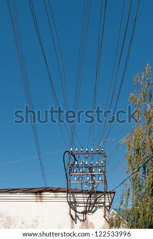 Power line wire bunch with insulators and metal framework on building roof against blue sky background.