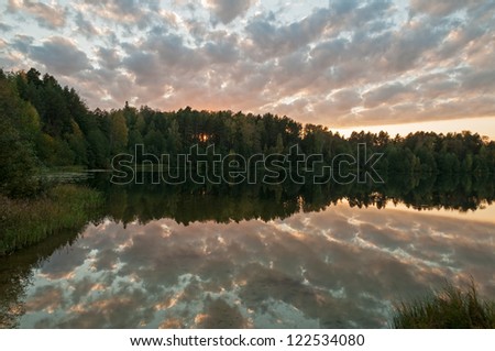 Sunset over Svetloyar Lake with bush in foreground and forest along bank reflecting in calm water