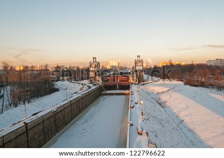 Closed shipping lock of frozen canal against city landscape background. Moscow, Russia.