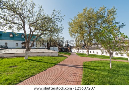 Buildings and wooden tower of ancient Transfiguration monastery with lawn, trees and paved road before against blue sky background. Novgorod-Siversky, Ukraine.
