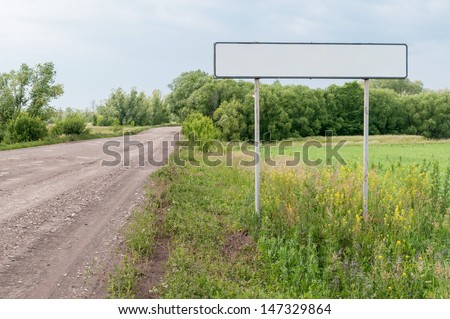 Straight road with white empty sign on roadside at the entrance to the city against beautiful summer landscape background. Bolshaya Doroga village, Tambovsky region, Russia.