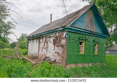 Old abandoned green wooden house with porch and broken windows among wild tall weeds. Bolshaya Doroga village, Tambovsky region, Russia.