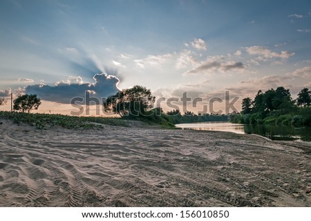Sand river beach and bush against sunbeams behind cloud background in back lighting