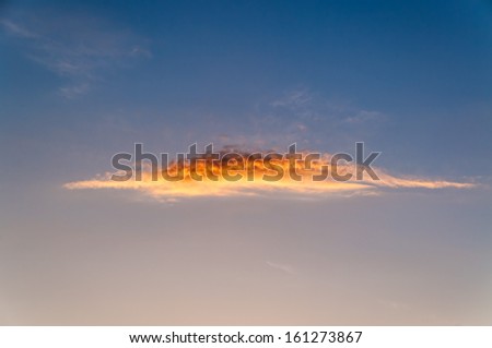 Beautiful oblong cloud with bright sun glow against blue sky background at sunset