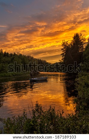 Beautiful bright dramatic sunset over river with man standing on his feet in boat and forest along riverside. Arkhangelsky region, Russia.