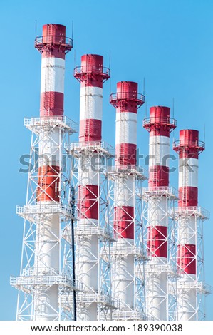 Red and white heating plant pipes with rails and landings against blue sky background.