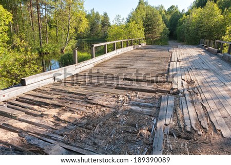 Old damaged wooden bridge with rails over river against forest background. Karelia, Russia.