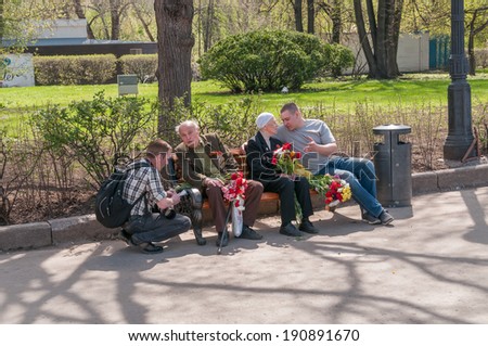 MOSCOW/RUSSIA - MAY 9: Two people talk to World War II veterans sitting with bunch of flowers on bench in Gorky Park during festivities devoted to Victory Day on May 9, 2013 in Moscow.