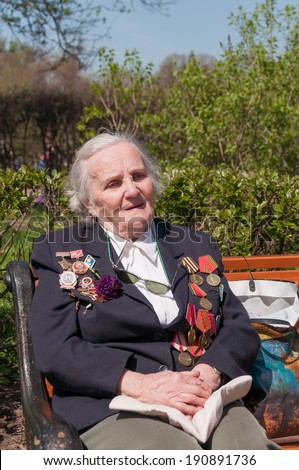 MOSCOW/RUSSIA - MAY 9: Old woman veteran of WWII in black coat decorated with numerous orders and medals sits on bench during festivities devoted to Victory Day on May 9, 2013 in Moscow.