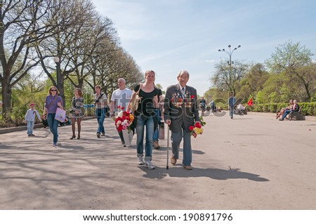 MOSCOW/RUSSIA - MAY 9: Old man veteran of WWII decorated with numerous orders and medals escorted by young woman walks in Gorky Park during festivities devoted to Victory Day on May 9, 2013 in Moscow.