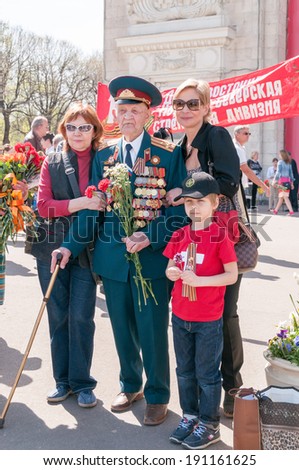 MOSCOW/RUSSIA - MAY 9: Old man veteran of WWII in uniform decorated with numerous orders and medals stands with Gorky Park visitors for common photo in Victory Day on May 9, 2013 in Moscow.
