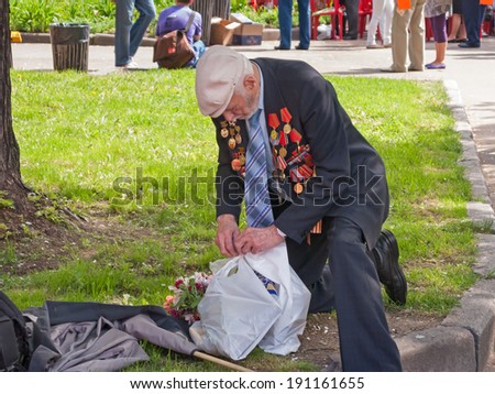 MOSCOW/RUSSIA - MAY 9: Old man veteran of WWII decorated with numerous orders and medals bends the knee on grass to collect his belongings in Victory Day on May 9, 2010 in Moscow.