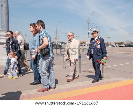 MOSCOW/RUSSIA - MAY 9: Old man veteran of WWII in uniform decorated with numerous orders and medals walks with bunch of flowers during festivities devoted to Victory Day on May 9, 2013 in Moscow.