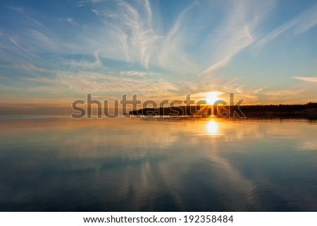 View on Onega Lake with bright Sun over distant cape and evening glowing reflecting in calm water at midnight sun. Karelia Republic, Russia.