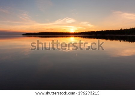 View on Onega Lake with bright Sun over distant cape and evening glowing reflecting in calm water at midnight sun. Karelia Republic, Russia.