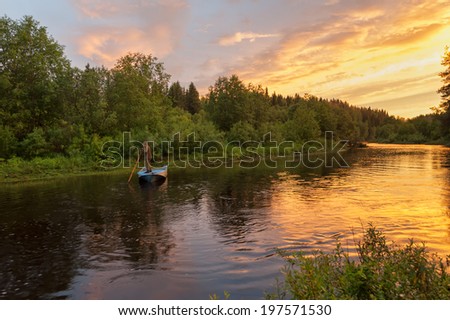 Beautiful bright dramatic sunset over river with man standing on his feet in boat and forest along riverside. Arkhangelsky region, Russia.