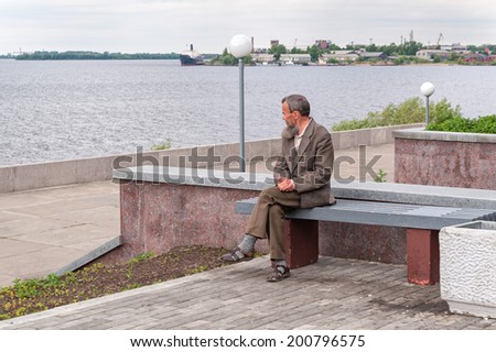 ARKHANGELSK/RUSSIA - JUNE 21: Old man sits on bench on embankment against Severnaya Dvina River and cloudy sky background on June 21, 2010 in Arkhangelsk.