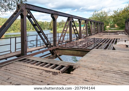 Disturbed rusty steel bridge above river in diminishing perspective. Nikolo-Uryupino village, Moscow, Russia.