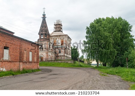 Ancient Spasoobydinskaya church (1697) with dirty road and old brick house before in Sun backlighting at sunset. Solvychegodsk, Arkhangelsky region, Russia.