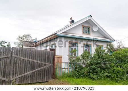 Beautiful white wooden house behind fence with decorative tin furnace accessories over chimney  against cloudy sky background. Solvychegods, Arkhangelsky region, Russia.