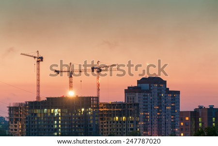 Tower cranes on construction site of modern buildings and skyscrapers against evening glow background. Moscow, Russia.