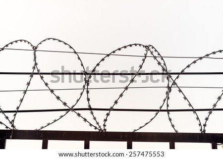 Heart shaped razor barbed wire over bar fence top on sky background close up view