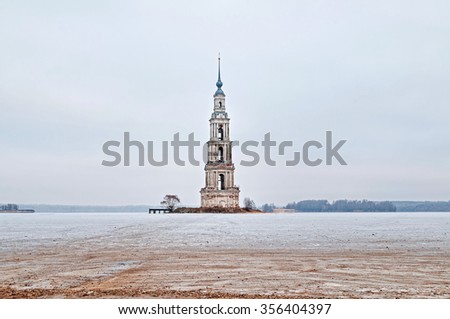 Winter view on the famous drowned belfry of St. Nicholas cathedral (1800) standing in middle of frozen reservoir against cloudy sky background. Kalyazin, Tverskaya region, Russia.