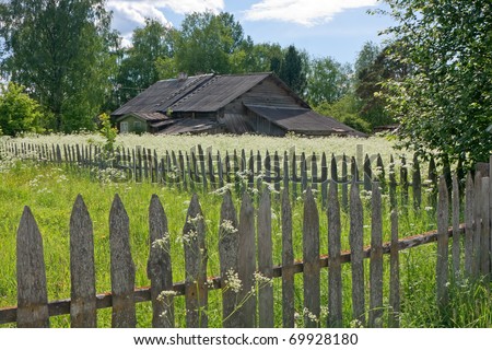 Old wood house buried in white flowers with fencing wood in foreground.