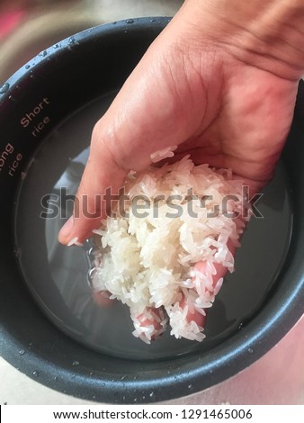 Hand washing grains of white rice in rice cooker pot.