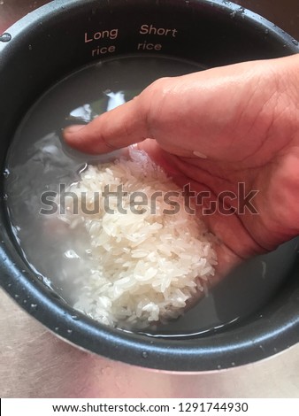 Hand washing white raw grains of rice in cooker pot.