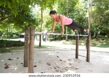 Beautiful woman doing dips exercise on balancing bar in park