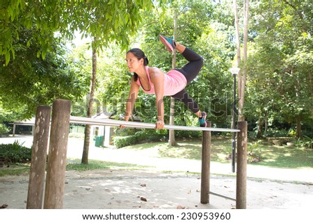 Beautiful woman doing dips exercise on balancing bar in park