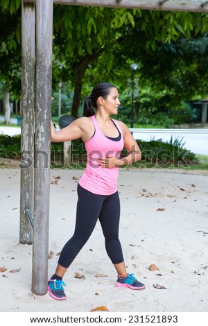 Sporty woman stretching upper arm by wooden post in exercise park