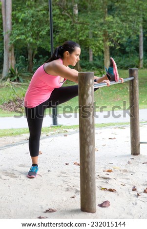 Sporty woman stretching inside of thigh on a bar, exercising in the park