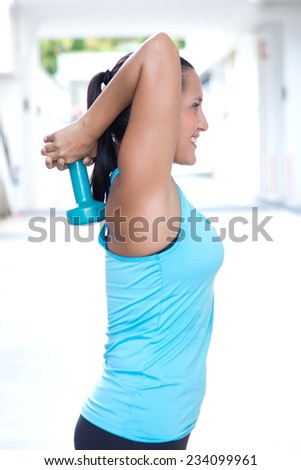 Sporty woman doing double extension with a dumbbel raised above and behind her head