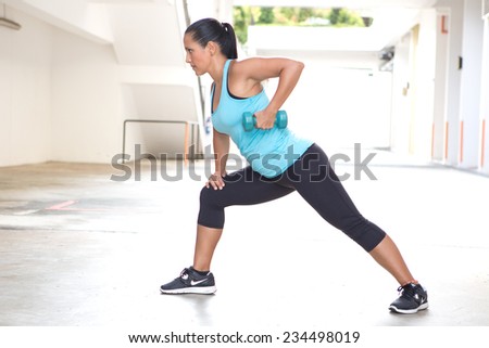 Beautiful sporty hispanic woman in blue  demonstrating the rowing routine with blue dumbbell outdoors