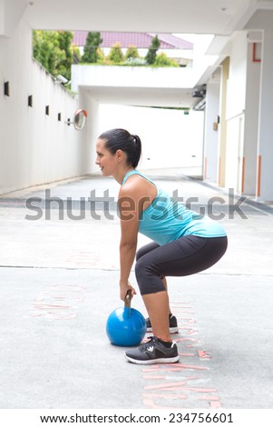 Beautiful sporty hispanic woman in blue attire holding a blue kettlebell in dead lift post outdoors