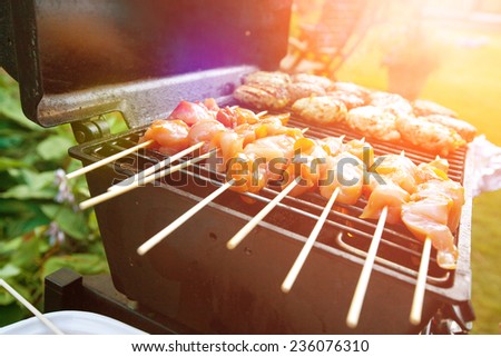 Sizzling burgers and chicken kebabs on hot barbecue outdoor in the evening sun.