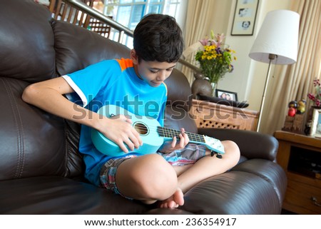 Young pan asian boy practicing on his blue ukulele in a home environment