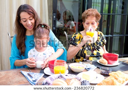 Beautiful hispanic family having breakfast together on the outdoor dining showing family bonding time. Focus is on child learning to drink milk.