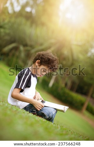 Young pan asian boy enjoying his reading book in outdoor park at sun down
