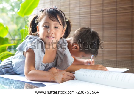 CuteÃ?Â??little pan asian girl smiling with a story book sitting next to an older brother engrossed in coloring activity in home environment