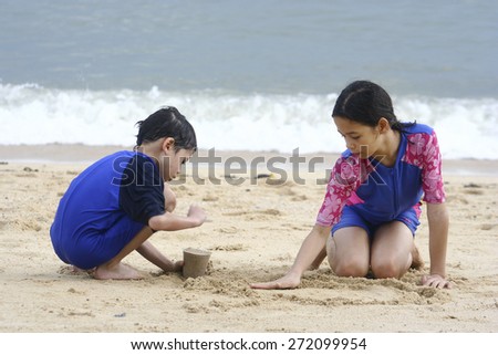 Young girl playing in the sand at the beach with younger brother