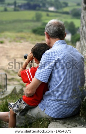 A child sits on his grandfather\'s lap while looking through a pair of binoculars Concept: Family love