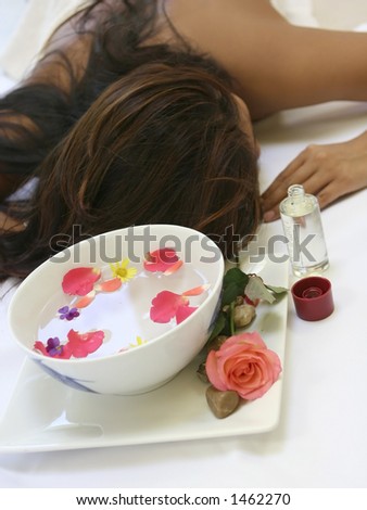 A woman awaits a sensual full body massage treatment showing a bowl of scented floral water and a bottle of massage oil
