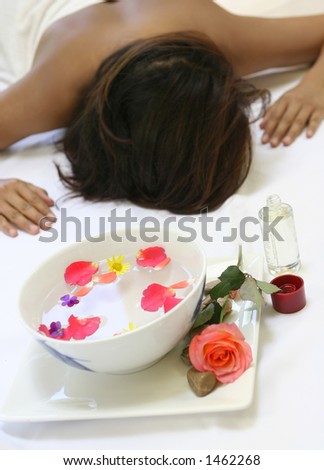 A woman awaits a sensual full body massage treatment showing a bowl of scented floral water and a bottle of massage oil