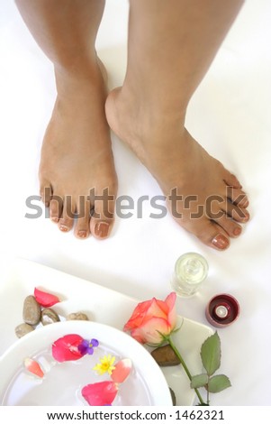 A setting for a  spa foot treatment showing a pair of feet, bowl of scented water with flower petals
